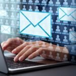 Hands typing on a laptop with floating blue email envelopes over a grid of user silhouettes.