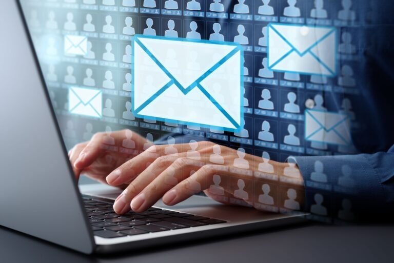 Hands typing on a laptop with floating blue email envelopes over a grid of user silhouettes.
