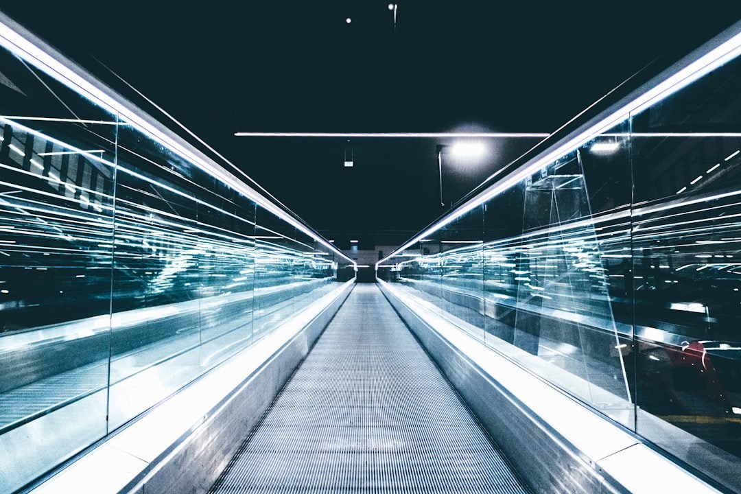Futuristic glass-walled moving walkway at night, blue neon lights reflecting off panels, perspective lines converging toward a distant vanishing point.